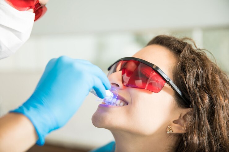 Closeup of young woman having her teeth whitened with ultraviolet light in a dental clinic<br />
